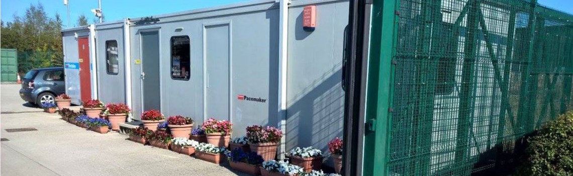 long grey portacabin office at a storage facility with colourful, welcoming flower tubs outside