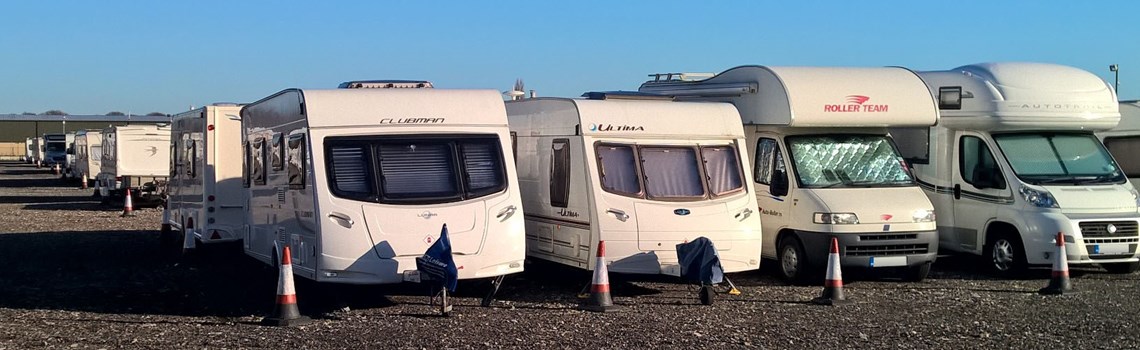 several rows of white caravans and motorhomes lined up in storage, with traffic cones marking their space